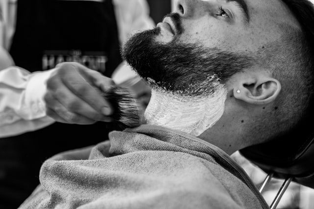 A barber shaving facial hair of a man