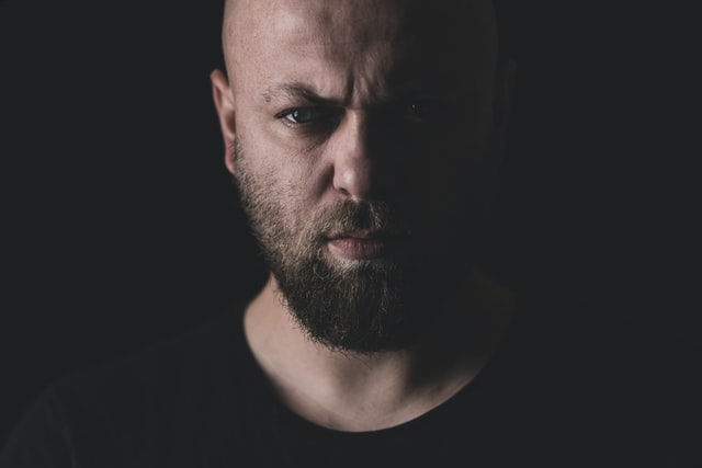 A close shot a bald headed man's face with beard in dark background