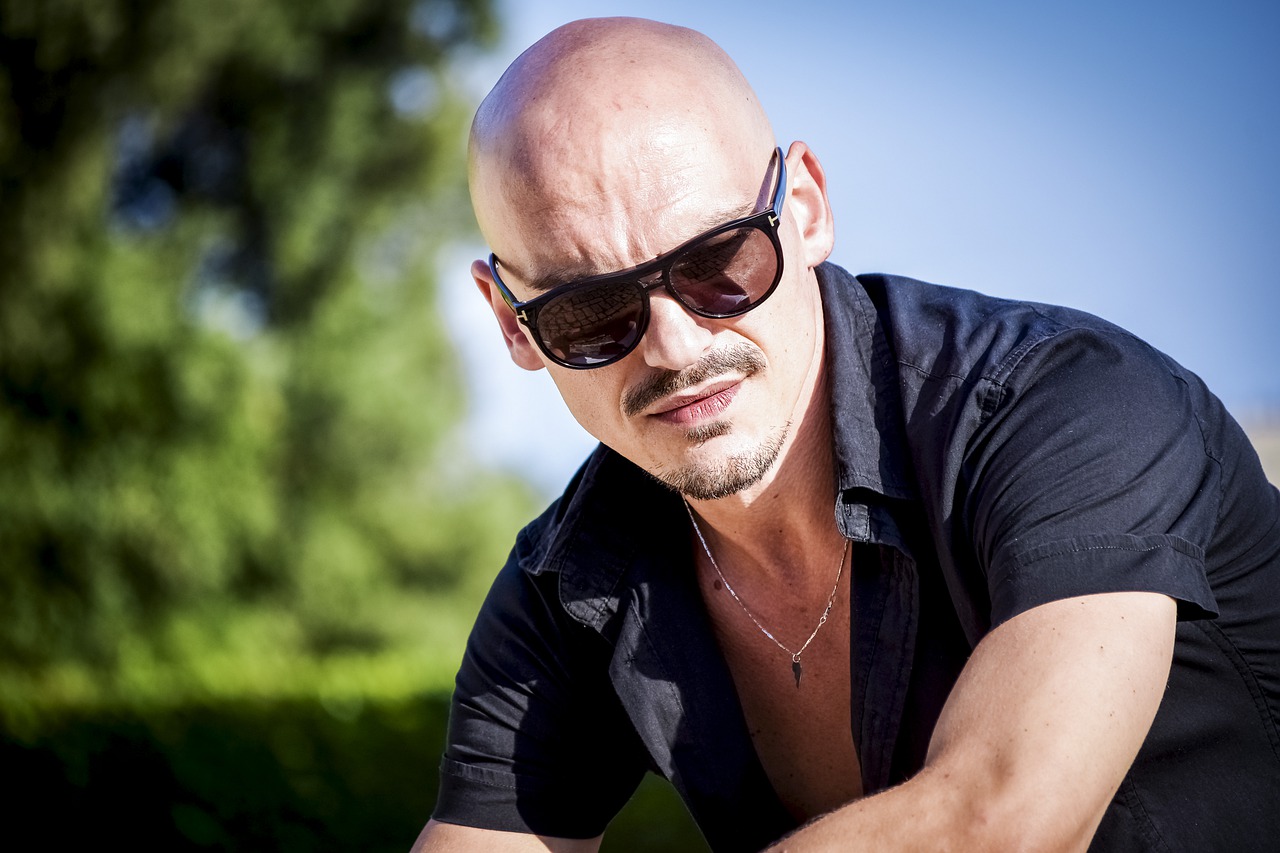 A portrait of a bald headed white man wearing black sunglass with black shirt
