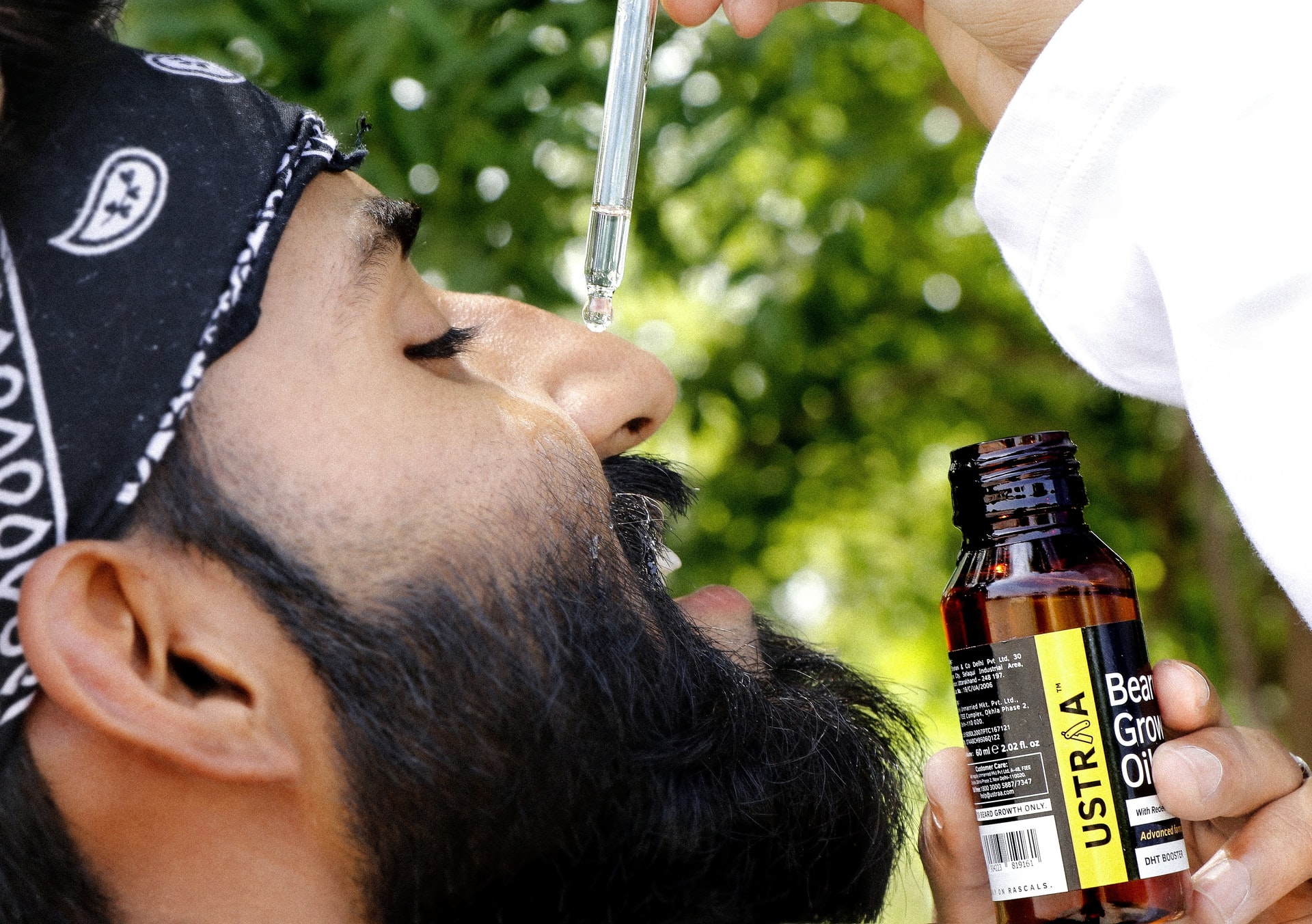 A bearded man applying oil into his beard using a dropper