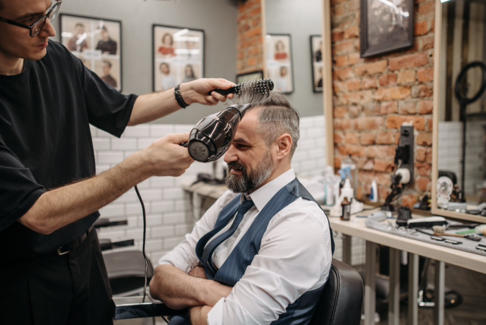 A barber blowing a man's hair with hair dryer at barber shop  