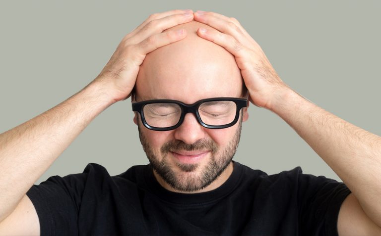 A man with a bald head puts his hands on his head closing eyes