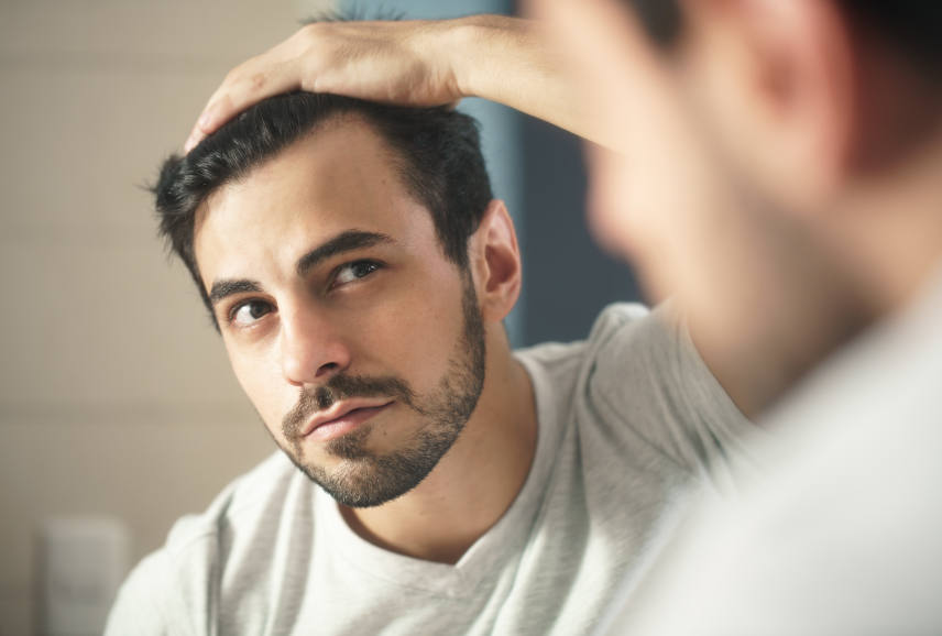 A bearded man checking  his receding hairline looking at mirror