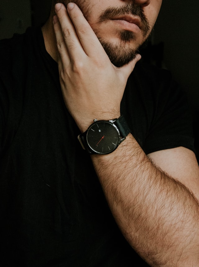 A man in black t-shirt checking his beard with his hand 