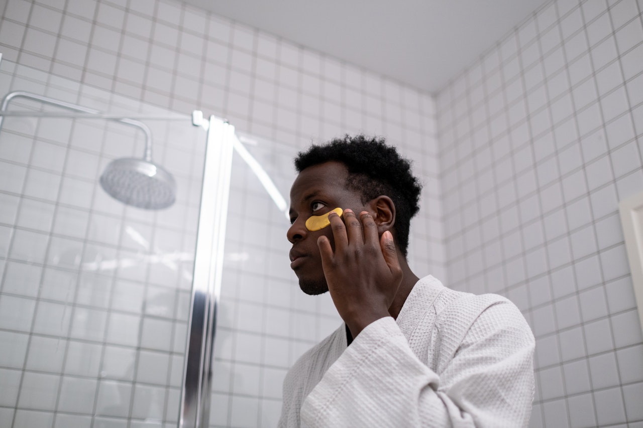 A black man applying cream under his eyes