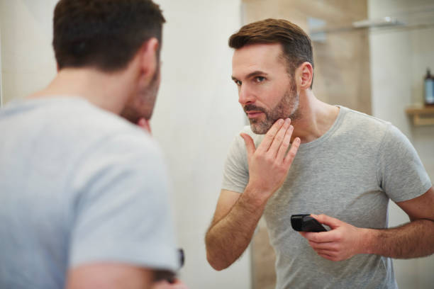 A man looking into mirror and checking his beard after self trimming