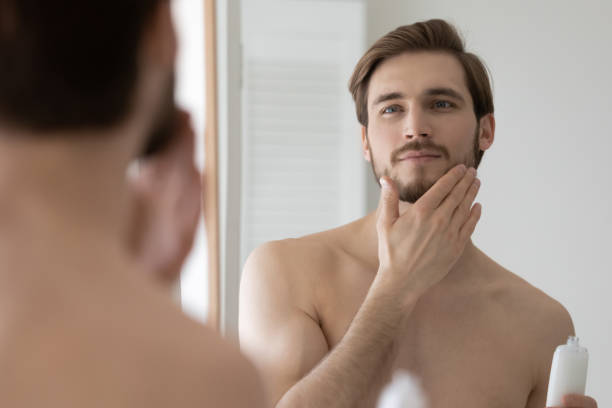 A young man applying lotion or balm on beard after-shaving or trimming