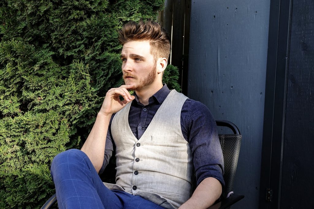 Portrait of a silky and golden colored hair man while sitting outside on a chair