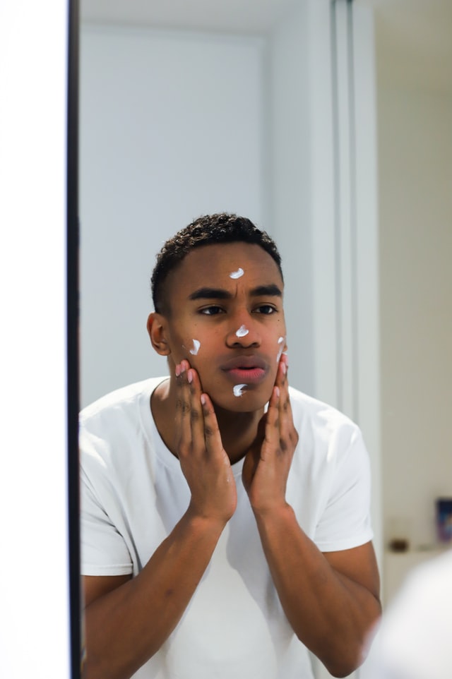 A black skin man applying cream on his face looking into mirror