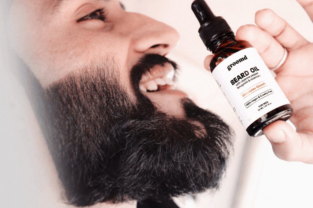 Portrait of a smiling beard man holding a beard oil bottle - advertising concept 
