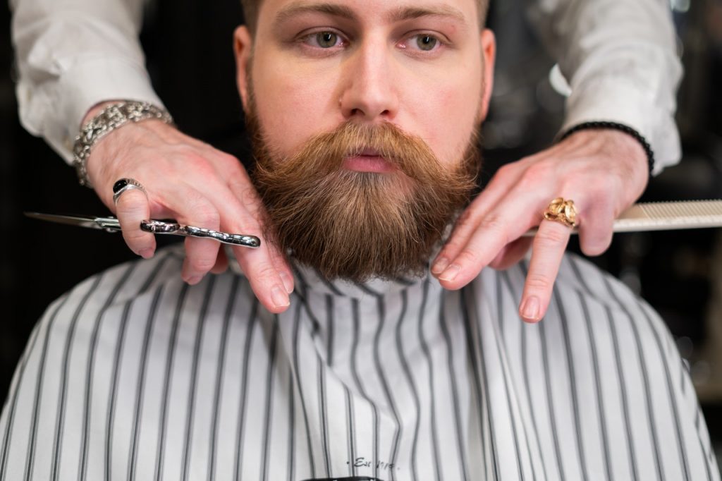 A barber trimming a man's mustache with scissors 