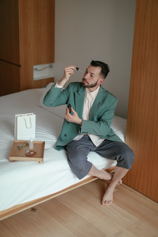 A man applying beard growth oil on his beard sitting inside bedroom