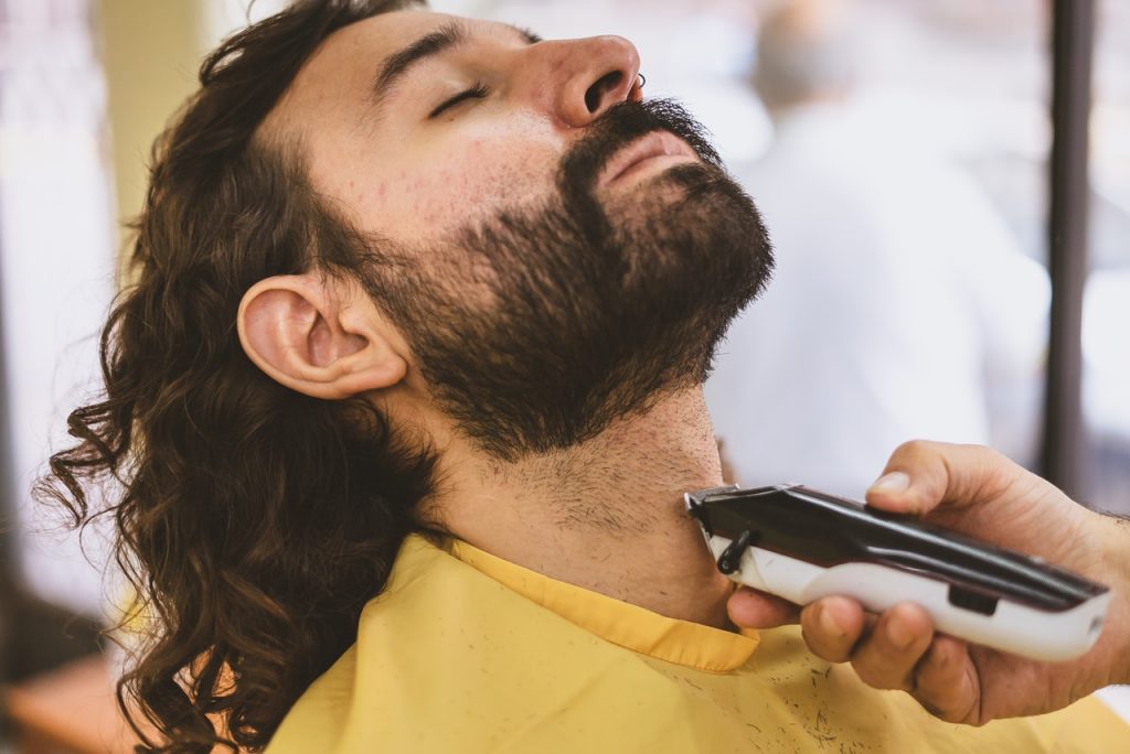 A long haired man getting trimmed his beard at barber shop