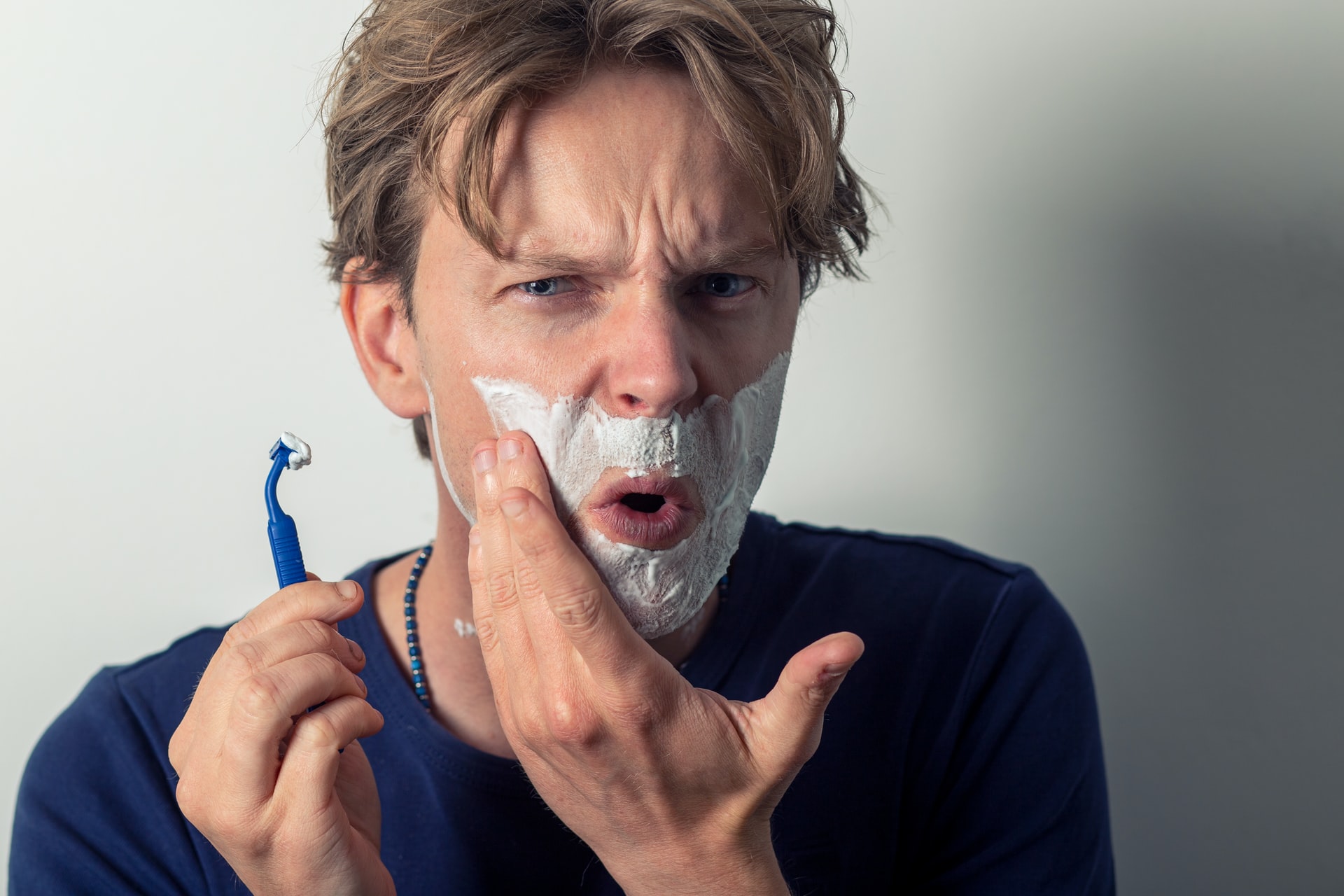 A man looking into mirror while shaving because of razor bumps 